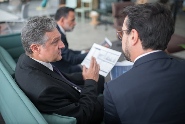 A person wearing a suit holding documents while talking to another person beside them